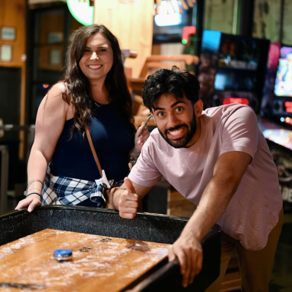 A Group Of People Standing Around A Table Playing Shuffleboard